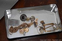 Mixed items in metal tray including money clip, brooch, chains and cufflinks