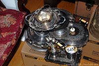 Photo showing stacked silver plated serving dishes including creamer, sugar bowl, trays, and spoons.