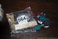 Photo of the lot items sealed in a plastic bag with a lot number tag, showing pearl necklaces and some badges/patches nearby.