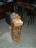 Front and side view of McVean croquet set with six mallets, six balls, metal wickets, and wooden stand on concrete floor.