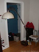 Full view of the metal floor lamp with curved arm and white glass dome shade in a room.