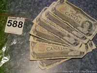 Ten 1967 Canadian one dollar bills fanned out on a blue surface, showing front side with Queen Elizabeth II and Canadian crest. Visible wear and creases.
