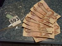 Seven 1986 Canadian two dollar bills shown fanned out on a surface with a MaxSold lot tag.