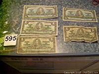 Photo showing two 1937 five dollar bills and three 1937 one dollar bills laid out on a surface, some wear and creasing visible.