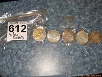 Five Canadian silver dollar coins placed side by side in plastic sleeves on a blue surface, with a MaxSold lot sticker nearby.