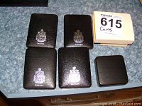 Five black leatherette coin cases with the Canadian coat of arms and a white cardboard storage box seen from above.