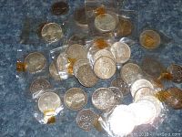 Overhead view of approx. 27 silver-colored coins on blue surface, many in plastic flips
