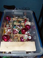 Wide view of plastic storage bin containing assorted vintage glass Christmas ornaments in various shapes and colors.