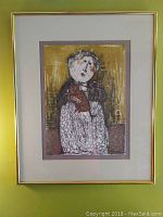 Front view of framed lithograph artwork showing a stylized figure holding an animal with double matting and gold frame.