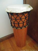 Side view of the tall ashiko drum showing wooden stave body with black rope tuning and natural hide drumhead.