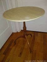 Full view of round wooden tilt top table with spider leg base, showing light natural wood finish and curved legs.