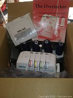 Photo of Baby Lock Protege overlock sewing machine inside the original box with instruction manuals and warranty card placed on top, sewing threads on spools installed on the machine.