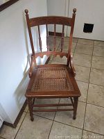 Full view of one Eastlake-style carved wooden chair showing cane seat with visible wear and detailed carvings on the backrest and legs.