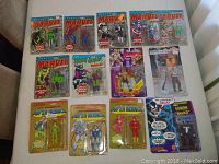 Collection of opened Marvel and DC Comics action figures displayed on a flat surface showing taped cardboard backing and visible character figures like Spider-Man and Hulk.