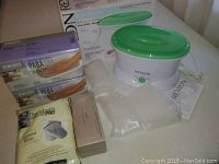 Overall lot showing Revlon paraffin bath with green lid, boxes of wax, glove liners, mitts, and protectors on a white surface.