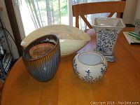 Front view of 3 vases and 1 large glass bowl on a wooden table with a chair and window in background