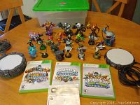 Photo showing about 20 Skylanders figures, 2 circular portals with cables, and 3 Xbox 360 game cases placed on a wooden table.
