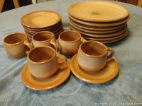 Photo showing stacked dinner plates and side plates with five matching mugs on saucers in front.