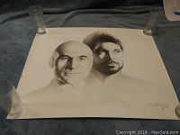 Print showing detailed black and white portraits of Captain Jean Luc Picard and Commander William T. Riker from Star Trek, laying flat with four cup-like objects weighing corners.