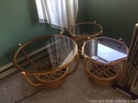 Three rattan tables grouped together: one oval coffee table with glass top, two side tables with round and hexagonal glass tops