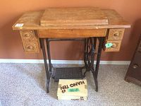 Full view of vintage Singer treadle sewing machine cabinet with wooden top and decorative side drawers, iron treadle base visible.
