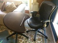 Photo showing office chair with black leather inner seat and back, armrests, and portable dark wood tilt writing table with ledge and 5 caster wheels.
