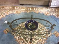 Full view of glass top metal coffee table with wrought iron base, showing the blue bowl with stones on the lower shelf
