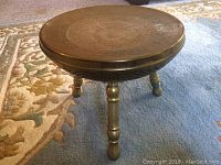 Full view of the round brass stool showing its three legs and the overall form.