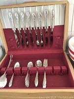 Full view of the silverware in case showing six knives in the lid and other pieces in bottom compartment.
