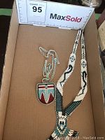 Two Native American beaded necklaces displayed in a box; one with a large pendant and patterned strap, one with a smaller pendant.