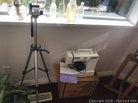 Full view of the sewing machine placed on its Janome RX 18S box with instruction manual and foot pedal visible. Vivitar tripod standing beside it.
