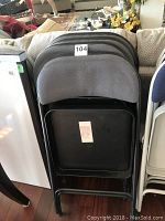 Stacked side view of folded metal frame chairs with gray upholstered backs, numbered 104 on top chair.