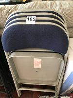 Four stacked folding chairs showing the beige metal frames and dark blue upholstered backs.
