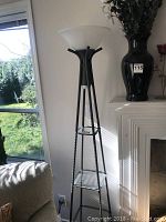 Full view of the pyramid floor lamp with three glass shelves and frosted white globe lampshade near a window and fireplace.