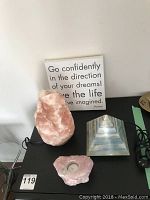 Pink Himalayan salt rock lamp, multi-color stone pyramid, and pink stone tea light holder arranged together on a surface with a text sign in the background