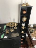Overview of brass collectibles displayed next to black multi-shelf unit, includes figurines, bowls, and decorative items.