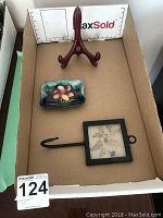 Wide view of lot showing both the Moorcroft dish and dried floral wall hook with stand inside a cardboard box.