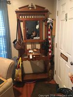 Full view of the wooden hall tree coat rack with multiple bags hanging on hooks and placed underneath.