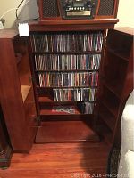 Front view of CD rack cabinet with doors open, showing many CDs stored on multiple shelves and additional shelves inside both doors.