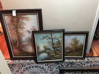All three framed landscape paintings displayed together on a floor rug, showing size scale and arrangement.