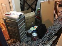 Overview of the lot showing storage drawer unit, bulletin boards, file folders, blank CDs, and other office items next to a doorway on a patterned carpet.