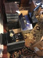 Overall view of lot including plastic storage drawers, monitor, printer, office supplies in boxes, and back massager on carpeted floor.