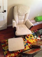 Front view of cream rocking chair and matching foot stool on colorful rug in room.