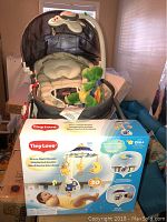 Tiny Love 3-in-1 rocking infant seat with cozy padding and plush headrest, Starry Night Mobile box placed in front, green plush turtle toy inside seat.