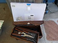 Photo showing open wicker garden toolbox with gardening tools inside and unopened box in background.