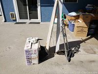 Photo showing Spotbot rug cleaner box, folding ironing board, walker, and wheelchair parts outdoors on concrete surface.
