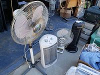 Wide shot showing all four items: large white standing fan, smaller white fan, white heater, and black Ionic Pro air purifier fan.