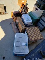 Overview of camping gear including picnic basket, coolers, chess board, sleeping bag, cardboard box, and storage bins.
