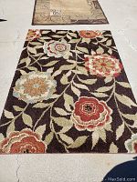 Area rug displayed flat on ground showing multicolor floral pattern on dark background.