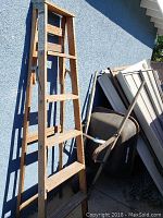 Photo showing full wooden 6-foot ladder and wheelbarrow leaning against blue wall.